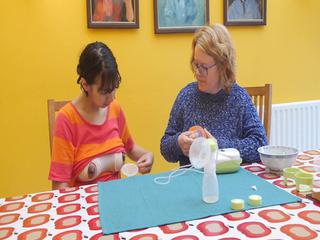 Ältere Frau zeigt junger Frau wie sie Milch aus ihren Brüsten pumpt